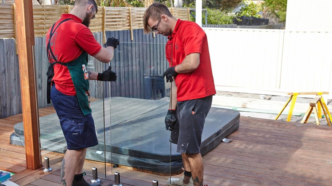 Two people putting glass pool fencing panel in place.
