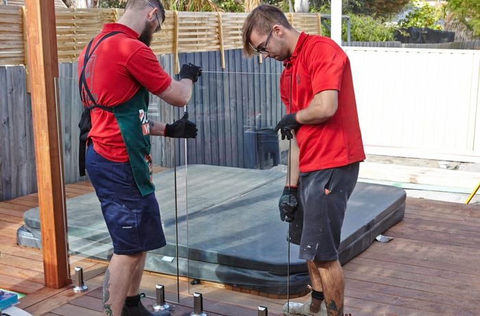 Two people putting glass pool fencing panel in place.