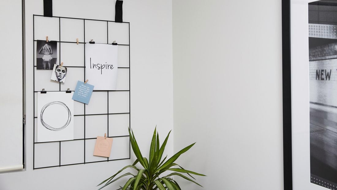 A wire mesh hanger on a wall containing a number of images and messages