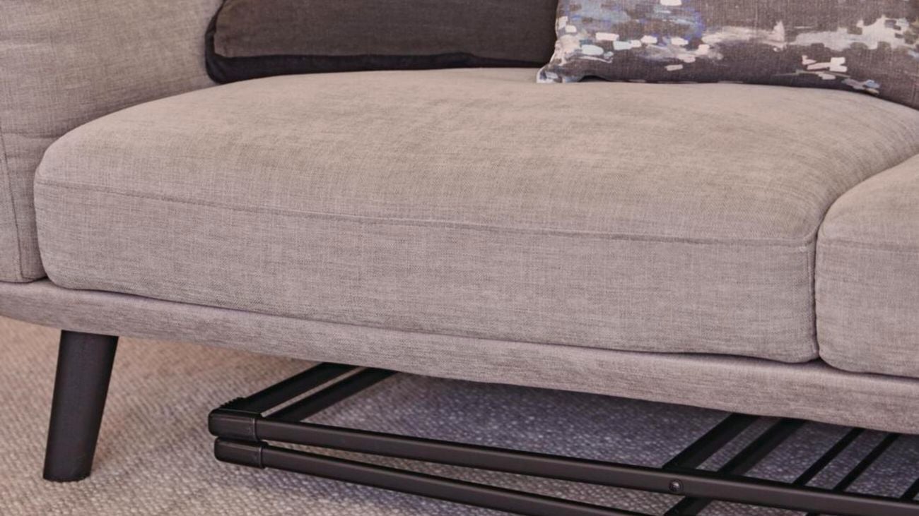 A clothes airer is folded down and stored underneath a sofa