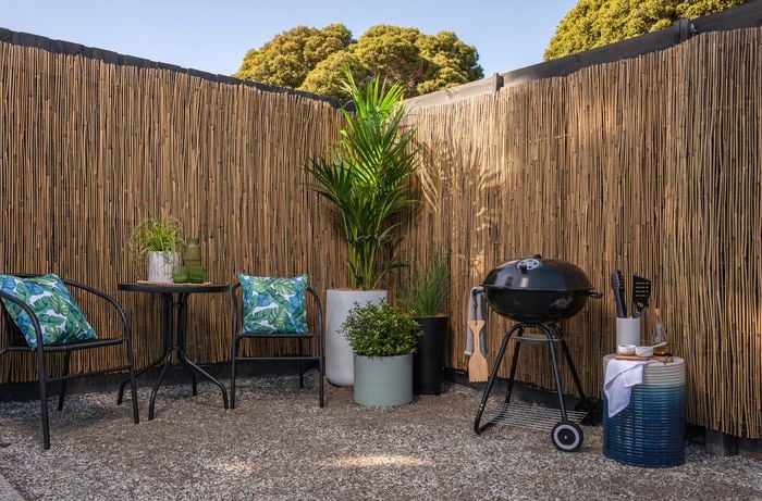 Outdoor chairs and table setup with barbeque and bamboo screen.
