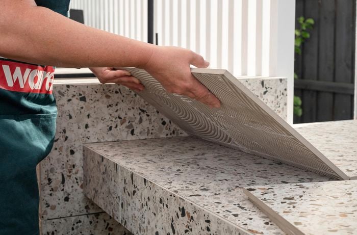 A person lifting an outdoor tile.