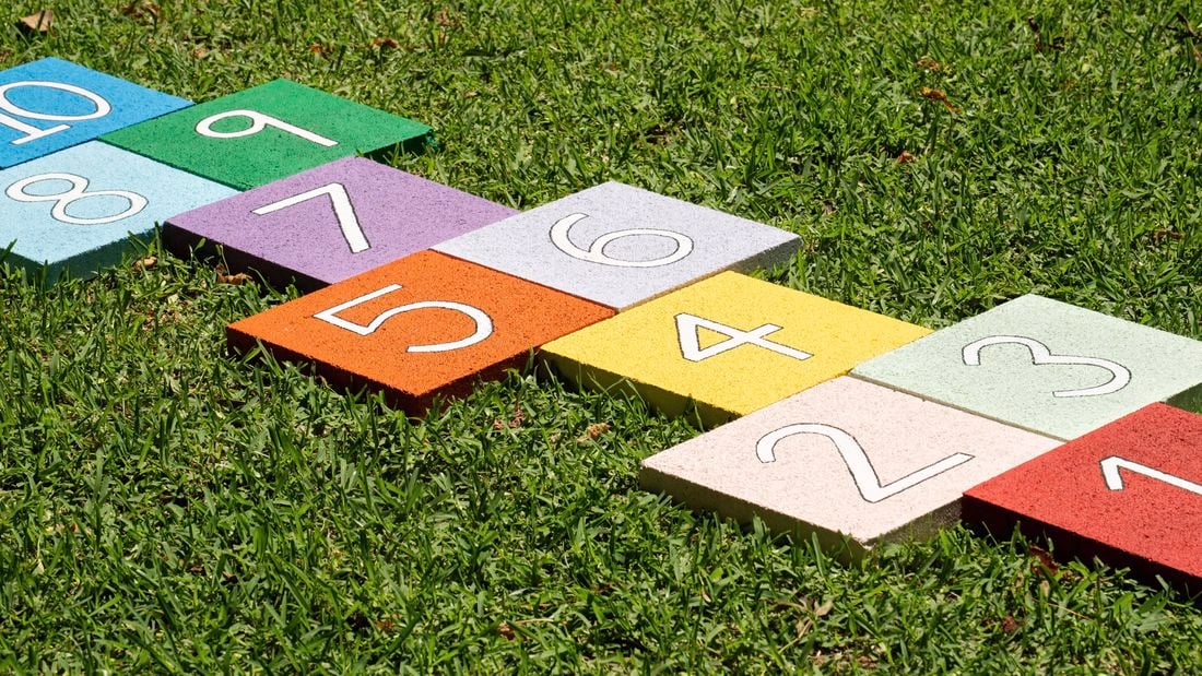 Colourful numbered paver tiles are placed on grass to create a reusable hopscotch path for outdoor family fun. 