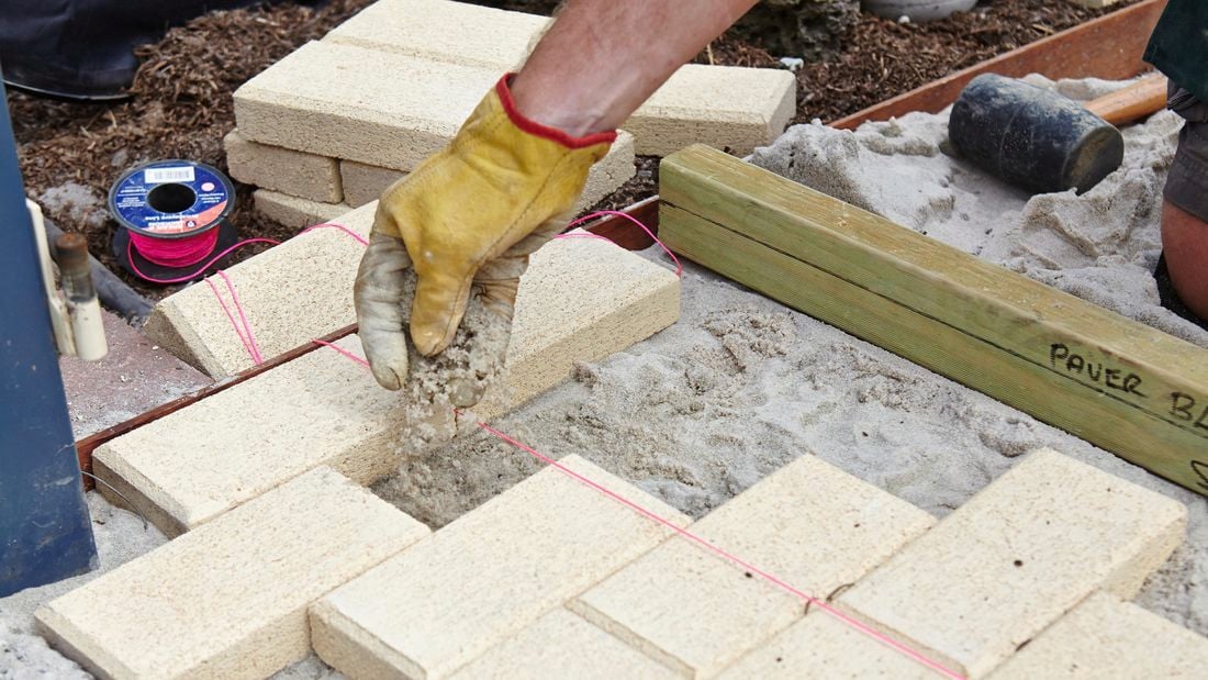 A person adding sand to a sand base between pavers