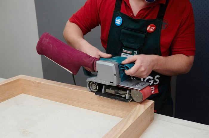 A wooden frame to be used as dining table legs being sanded with a belt sander