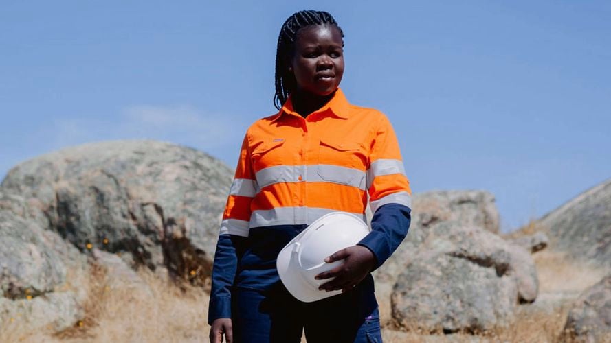 A lady wearing work site clothing and holding a white helmet.