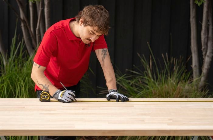 A Bunnings Team Member is measuring and marking a timber benchtop before cutting it to size.