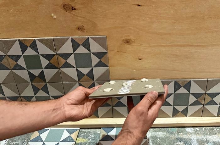 A close up of a two hands laying tiles on plywood bedhead