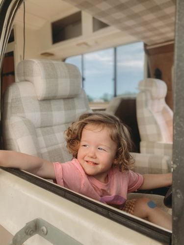 A child looking through an RV caravan window, smiling.