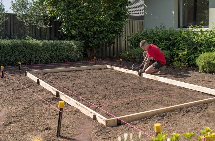 A Bunnings Team Member is using a hammer to secure concrete formwork, reinforcing it with steel posts to maintain its shape under wet concrete.  