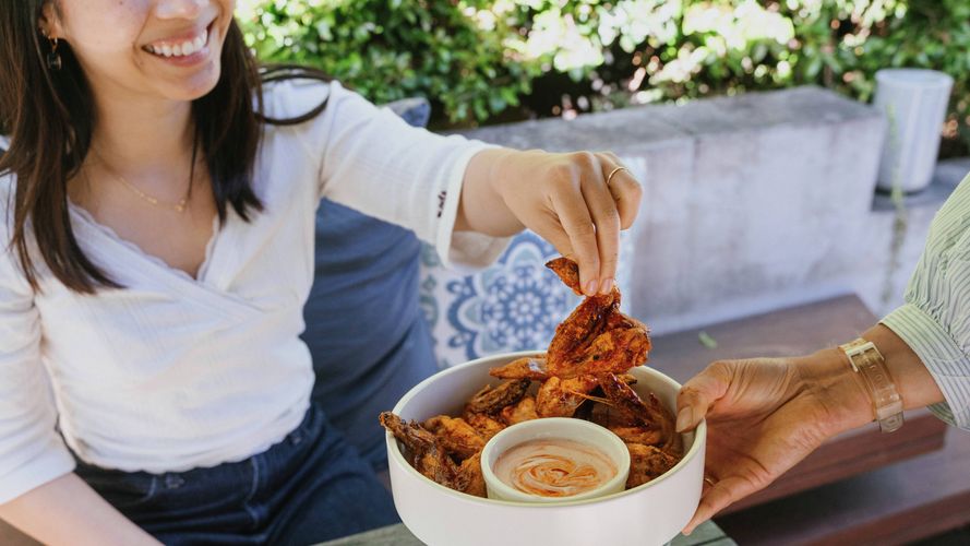 Person enjoying spicy chicken wings with dipping sauce at an outdoor table.