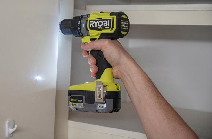 Image of a person's hand holding a electric screwdriver, while using it to remove the door handle from a surface.