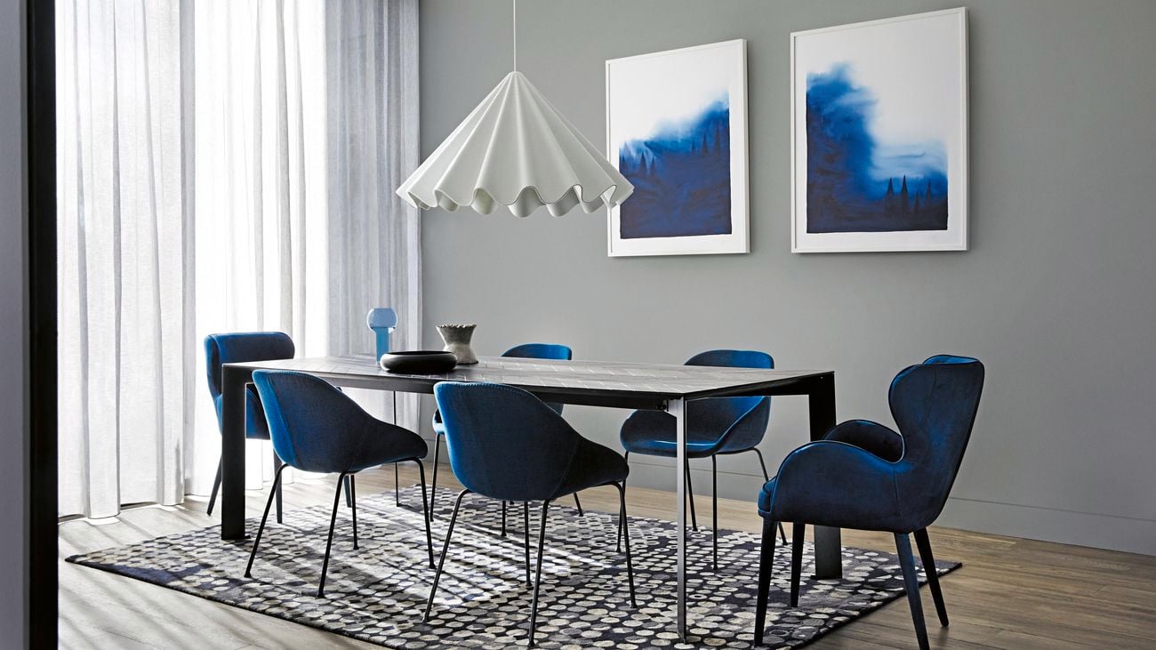 Dining room with blue velvet chairs and industrial table with a white hanging pendant and two large prints on wall