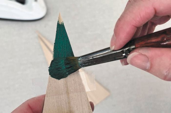 Hands use a paintbrush to paint paper green