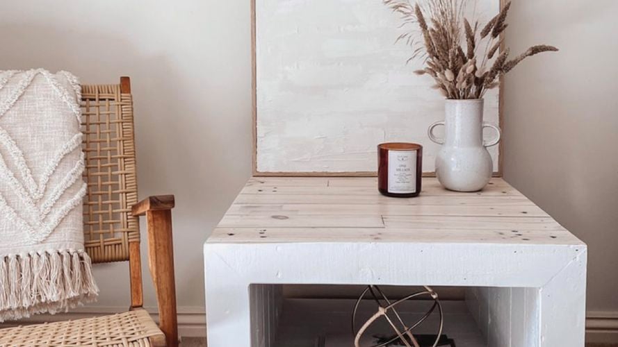 Chair and table with candle, fern plant, white painting and books. 