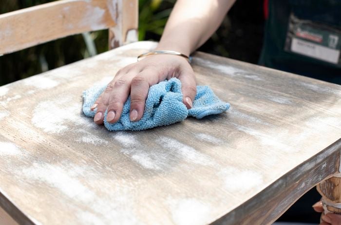 Person wiping old wooden dining chair with cloth.