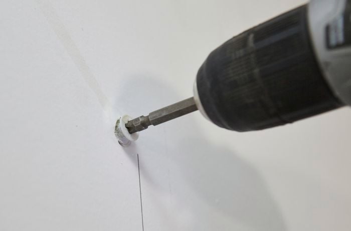 A screw being drilled into a plastic toggle in the wall in the absence of a wall stud