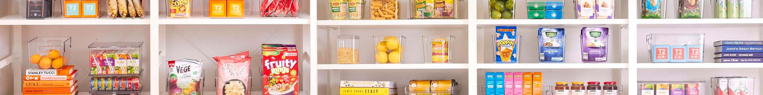 View of shelving with a variety of clear storage containers storing various food products arranged based on colour.