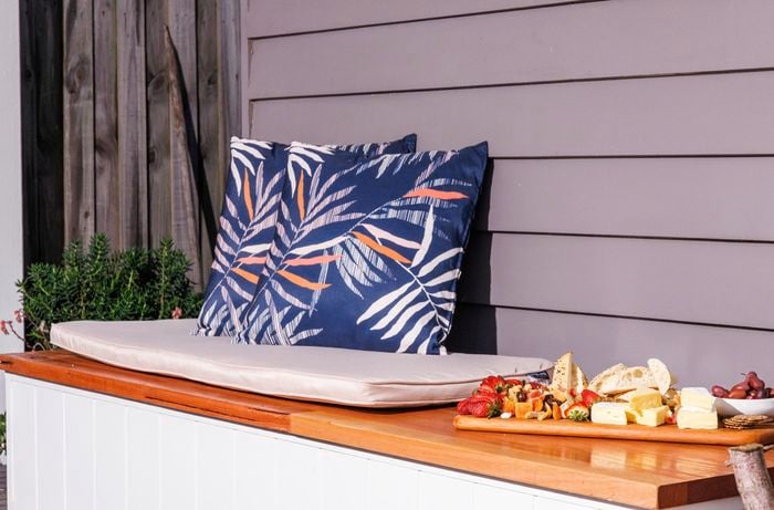 A decorated outdoor storage bench with two cushions and a fruit plater.