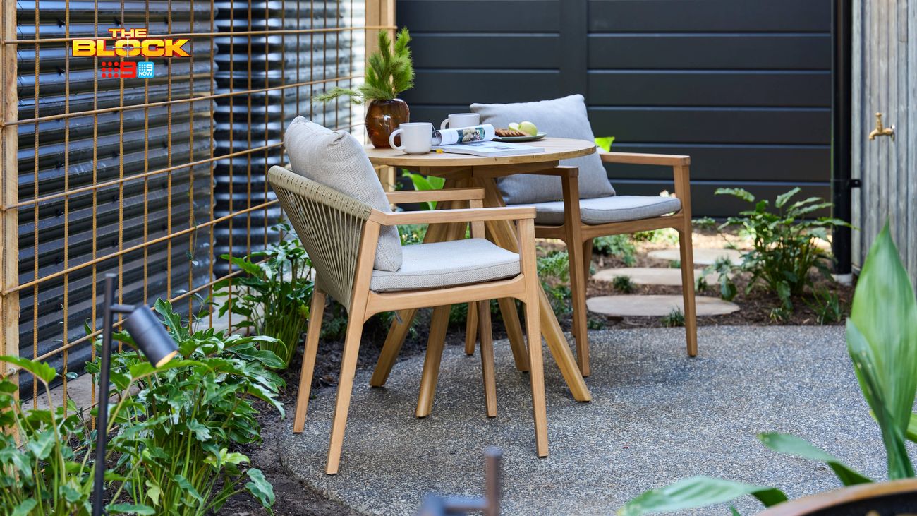 Outdoor courtyard featuring timber dining furniture with cushioned chairs, bamboo screening, dark fencing and landscaped garden beds.