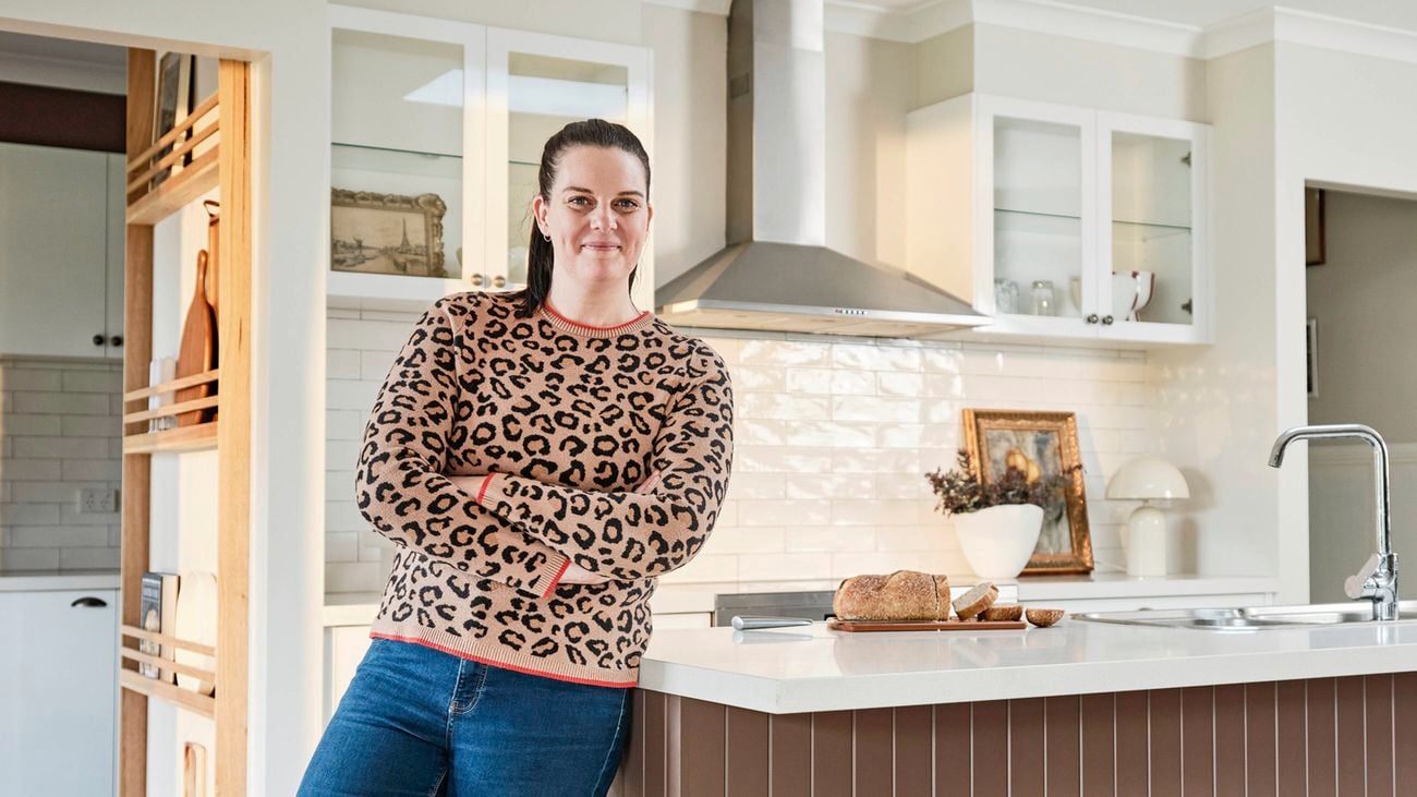 Person standing with arms crossed in a modern kitchen, leaning against a bench with sliced bread on the counter.