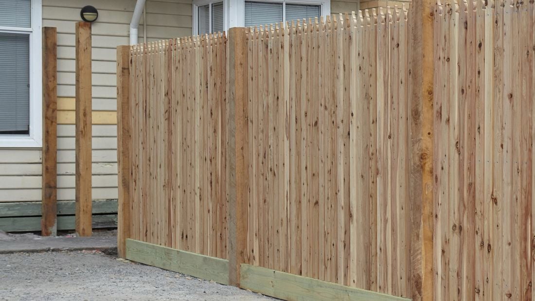 A completed wooden picket fence, surrounding the front yard of a suburban home
