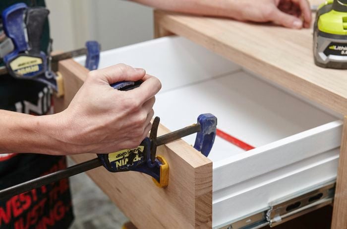A person clamping a piece of timber to the front of a drawer