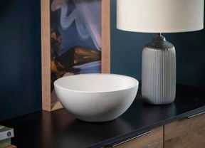white bowl sitting on a cabinet, with a  white lamp and print in the back ground