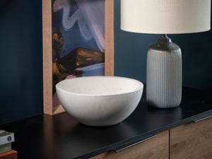 white bowl sitting on a cabinet, with a  white lamp and print in the back ground