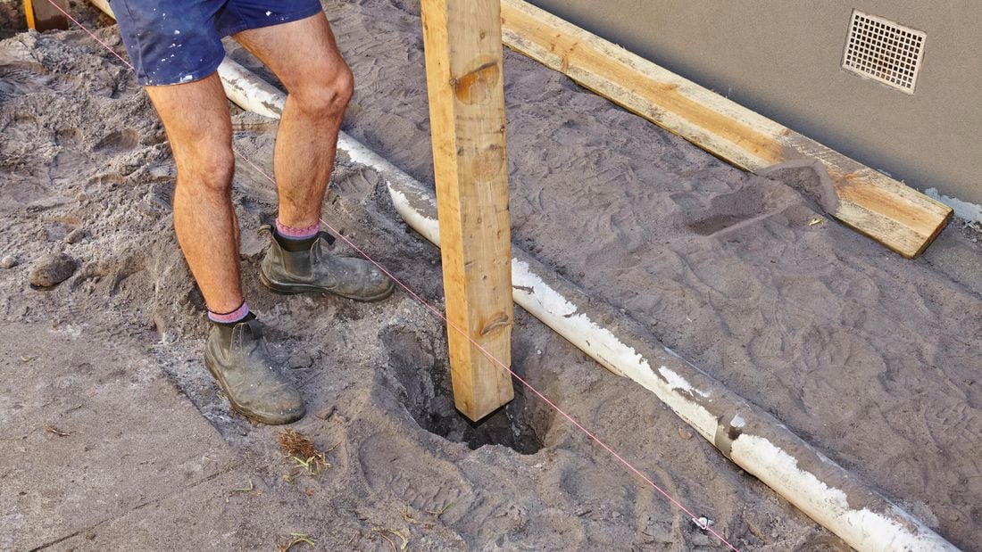 A fence post being lowered into a posthole marked out by string