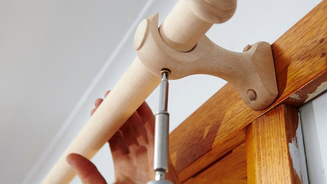 Person screwing curtain rod into curtain rod hook.