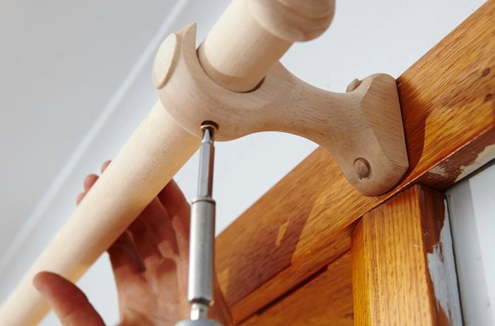 Person screwing curtain rod into curtain rod hook.
