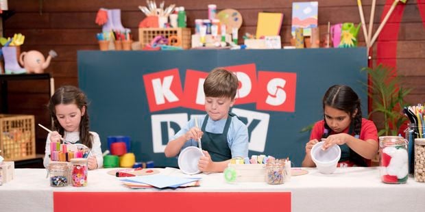 Three kids are sitting in a Bunnings DIY workshop, colouring pots