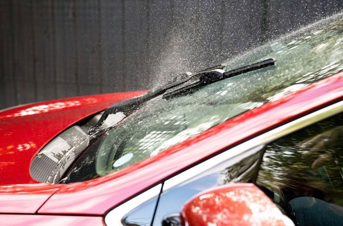 A red car’s windshield is sprayed with windscreen washer fluid.