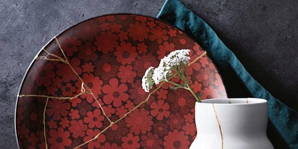 A cup, vase, and flower-patterned plate repaired with kintsugi techniques, each with a vein of gold running through