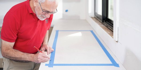 A Bunnings Team Member is marking the cut-out location on a laminate benchtop using a pencil and masking tape.
