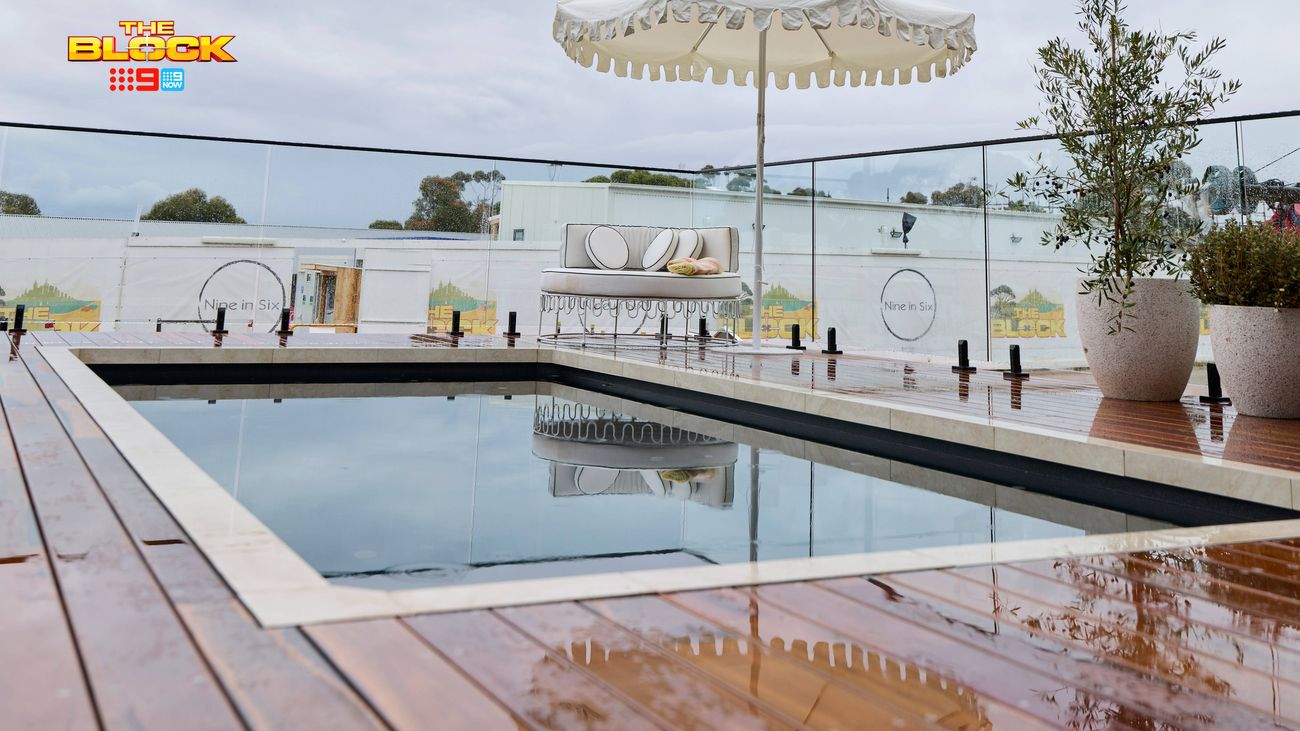 Outdoor pool area featuring wet timber decking, a decorative umbrella, glass balustrade and potted plants.