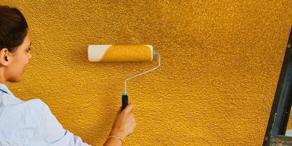 Using a paint roller to paint an external wall yellow