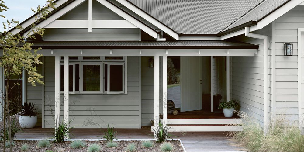 Grey house with white trim and dark corrugated iron roof, front porch with wooden deck, and garden.