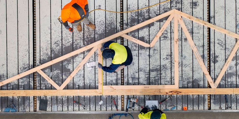 Trade men wearing fluor's  putting  together a timber frame in a work shop.