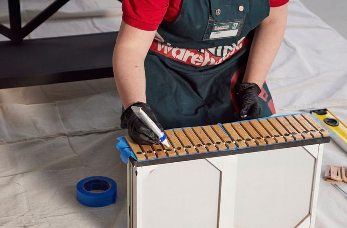 Person applying adhesive with a gun along wooden slats.