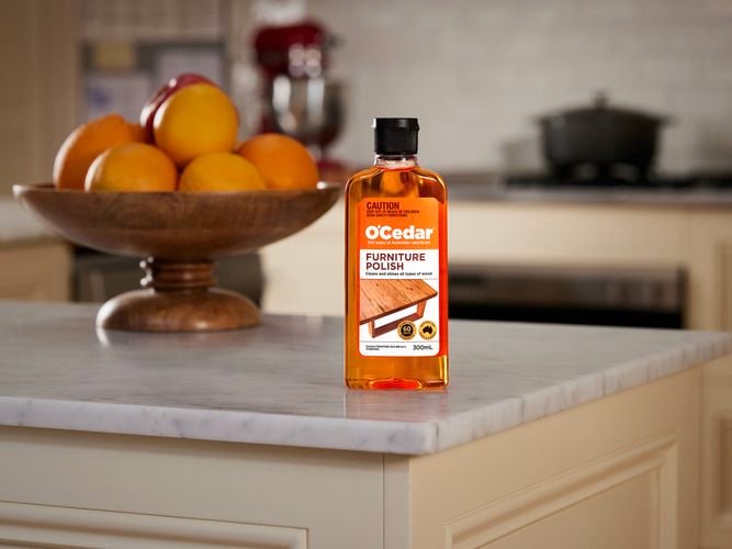 A bottle of O'Cedar Furniture Polish and a bowl with oranges in it on a kitchen bench top.