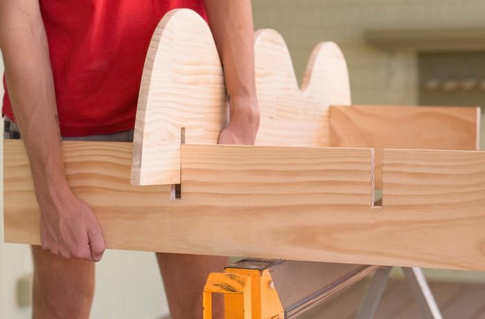 A person is testing the fit of the bookshelf panels by slotting in a wavy panel into notches on a horizontal board.