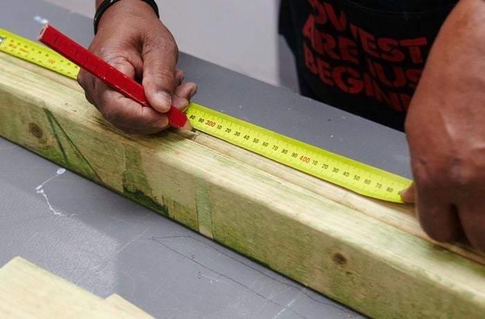 A pencil and tape measure being used to mark a length of wood