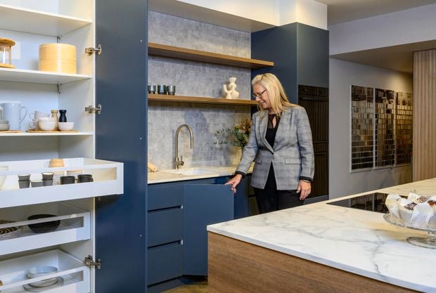 A lady in a kitchen with blue cupboards and a marble benchtop.