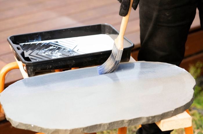  A person is using a paintbrush to apply a sealant onto tuscan path natural stone pavers.