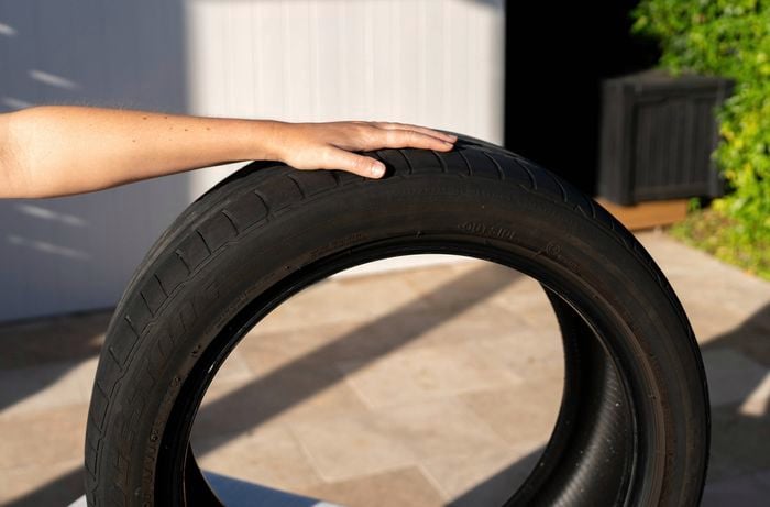 A person is holding a recycled tyre that is sitting on paving outside.