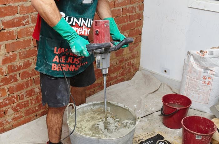 A person mixing cement plaster mix in a bucket using an electric mixer