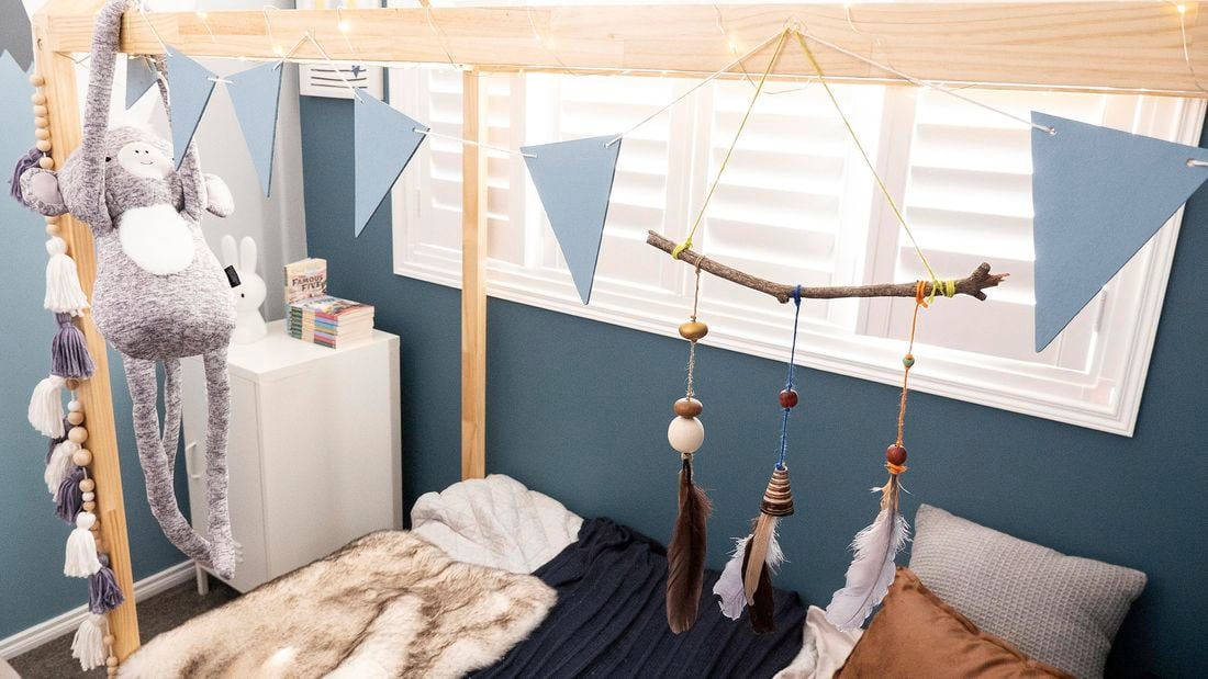 A nature hanging with sticks, beads and feathers, and a bunting hanging over a child's bed.