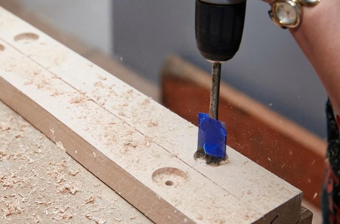 Person using drill with wide drill bit to create a hole in a piece of timber.